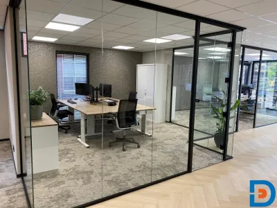 Kantoor met glazen wanden en een combinatie van pvc en tapijt, lichte kleuren en mooie werkplekken voor een frisse, open sfeer.