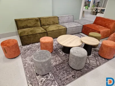 Gezellige zithoek in kinderopvang met zachte banken, kleurrijke poefjes en speelse accessoires op een zachte vloer met karpet