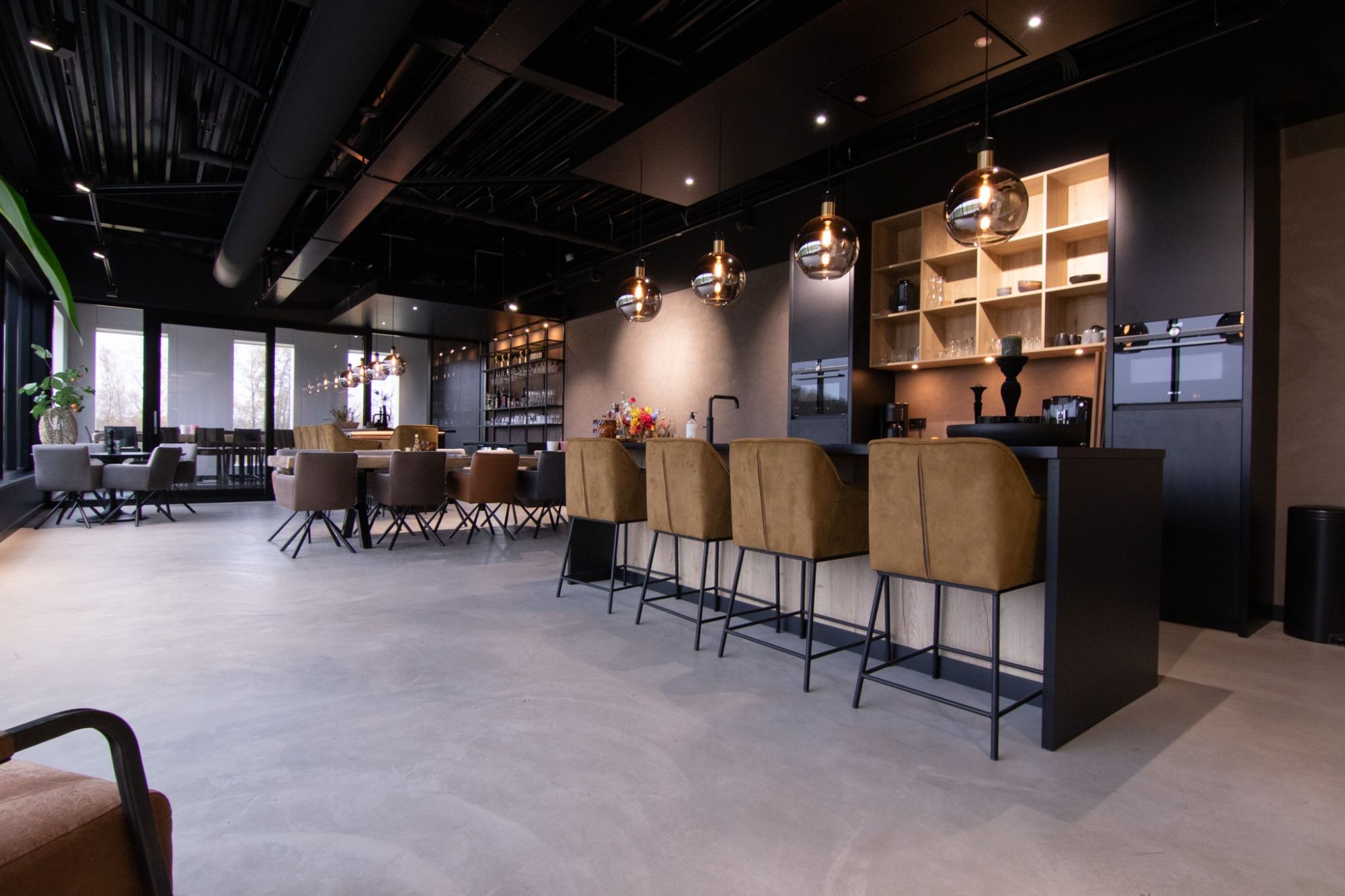 Moderne koffiecorner met bar, zitplekken en warme verlichting in een open kantooromgeving.