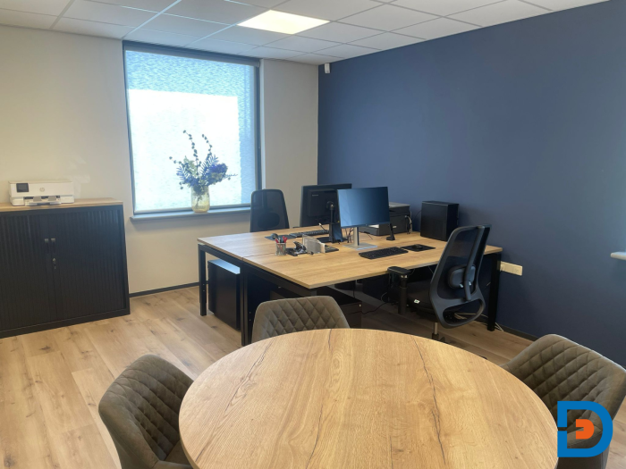 Een kantoorruimte ingericht met ergonomische bureaustoelen en een grote vergadertafel. Het ontwerp biedt een comfortabele en functionele werkplek met uitzicht op de buitenomgeving door de grote ramen.