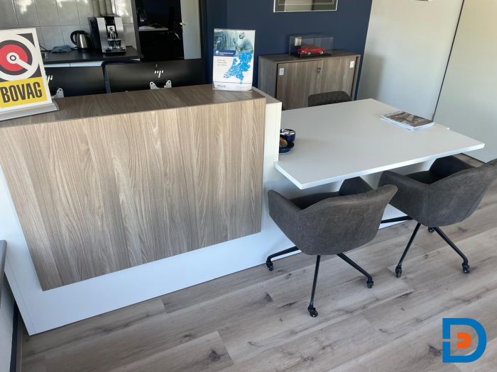 Ruimtelijk en moderne werkplek met een functionele balie en vergadertafel bij Goossen Autoschade, ideaal voor klantenontvangst en kort overleg.