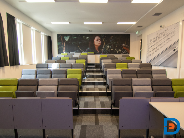Trapgewijs ingerichte collegezaal met kleurrijke klapstoelen en sfeervolle wandafbeelding.