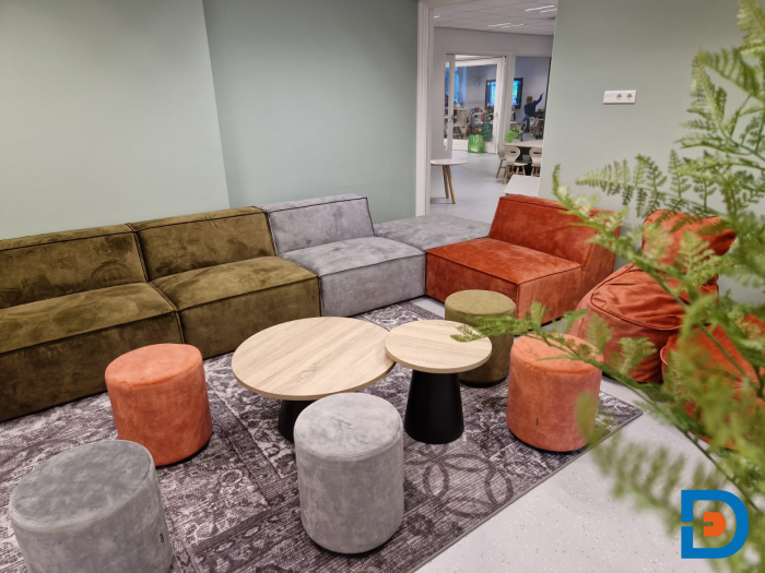 Zithoek in kinderopvang met zachte banken, kleurrijke poefjes, ronde tafeltjes en een huiselijke sfeer.