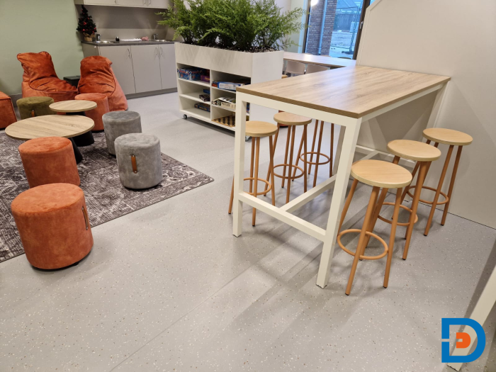 Personeelsruimte met een eetbar, houten krukken en kleurrijke poefjes voor een ontspannen werksfeer.