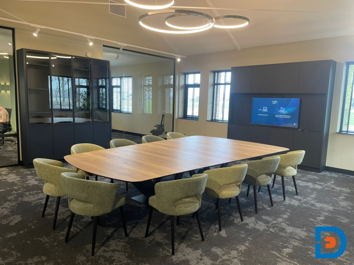 Vergaderruime met ringlampen en een grote vergadertafel en gestoffeerde stoelen groen