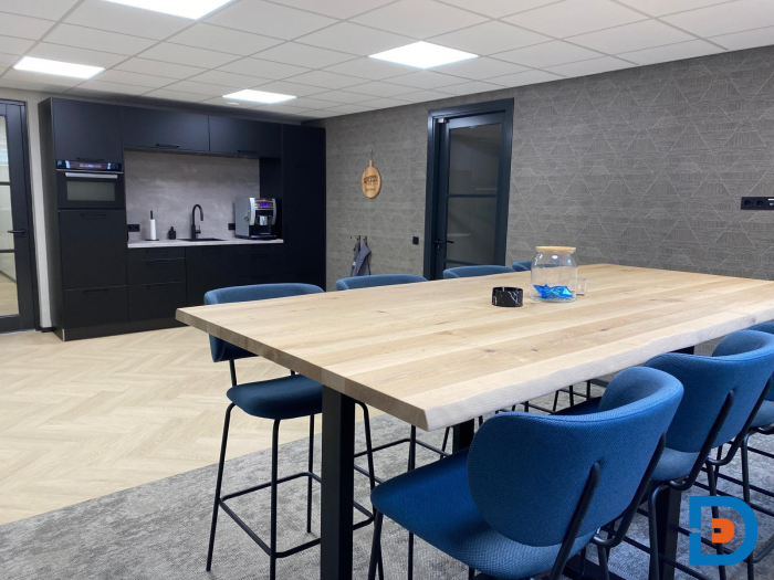 Functionele maatwerkkeuken met sfeervol behang en visgraat PVC-vloer, aangevuld met comfortabele gestoffeerde krukken rondom een robuuste houten statafel.