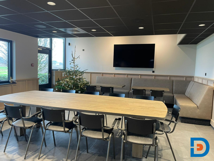 Personeelsruimte met een lange houten tafel, comfortabele stoelen en treinbanken, geschikt voor groepsvergaderingen en discussies of pauzes.