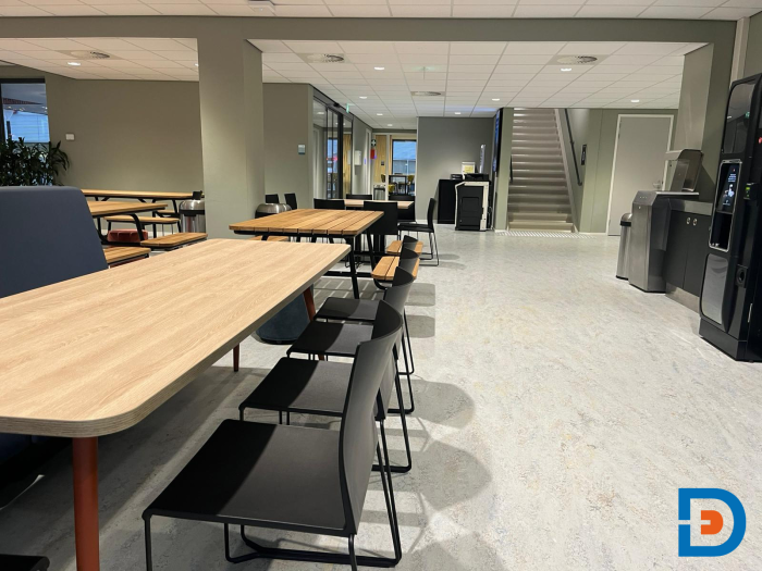 Moderne eetruimte met lange tafels, stoelen en een open ruimte, ideaal voor groepsmaaltijden en informele vergaderingen bij ROC Almelo.