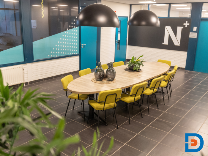 Moderne ovale tafel omringd door gestoffeerde stoelen in de herkenbare kleuren van de huisstijl.