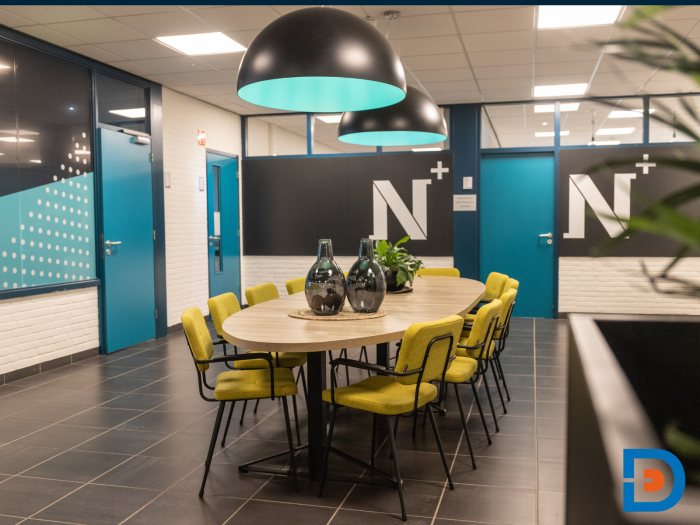 Moderne ovale tafel omringd door gestoffeerde stoelen in de herkenbare kleuren van de huisstijl.