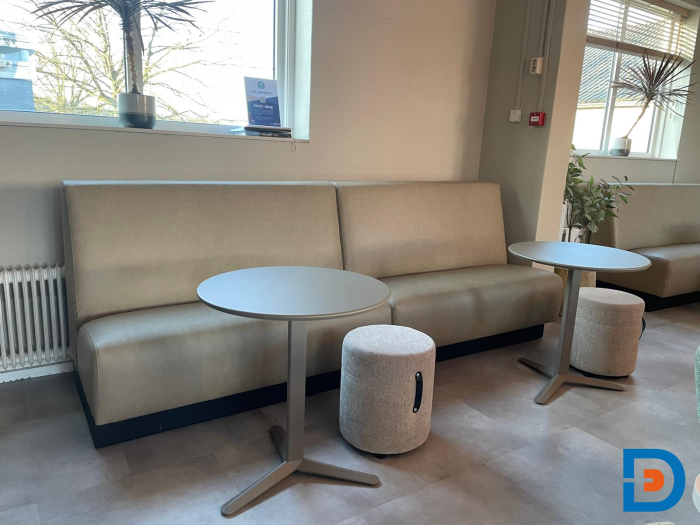 Zithoek in personeelskamer met lichtgroene treinbank, ronde tafels, krukjes en veel daglicht.