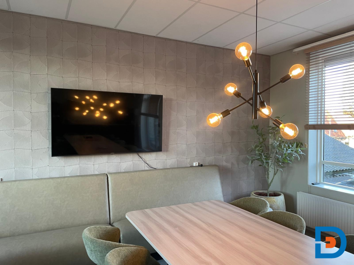 Moderne personeelskamer met lange tafel, wandtreinbank, televisie, designlamp en natuurlijk licht.