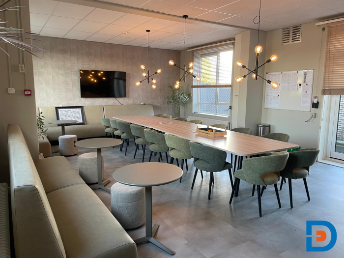 Lichte personeelskamer met lange vergadertafel, zithoek, ronde bijzettafels en moderne verlichting.