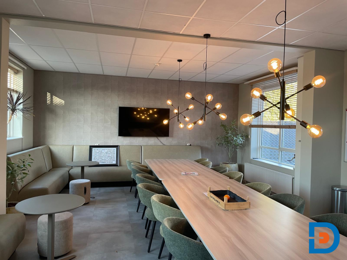 Lichte personeelskamer met lange houten tafel, moderne hanglampen, zithoek en natuurlijke accent