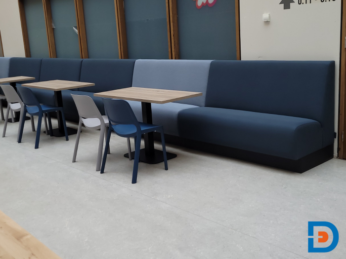 Makkelijk te plaatsen treinbanken gecombineerd met kolomtafels en stapelbare stoelen voor een praktische kantine-inrichting.