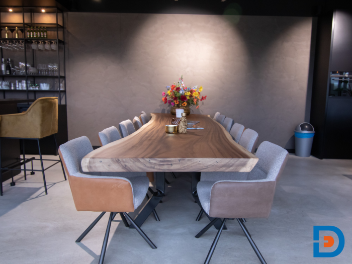Unieke boomstamtafel in de kantine, omringd door comfortabele, gestoffeerde draaistoelen voor een warme en uitnodigende sfeer.